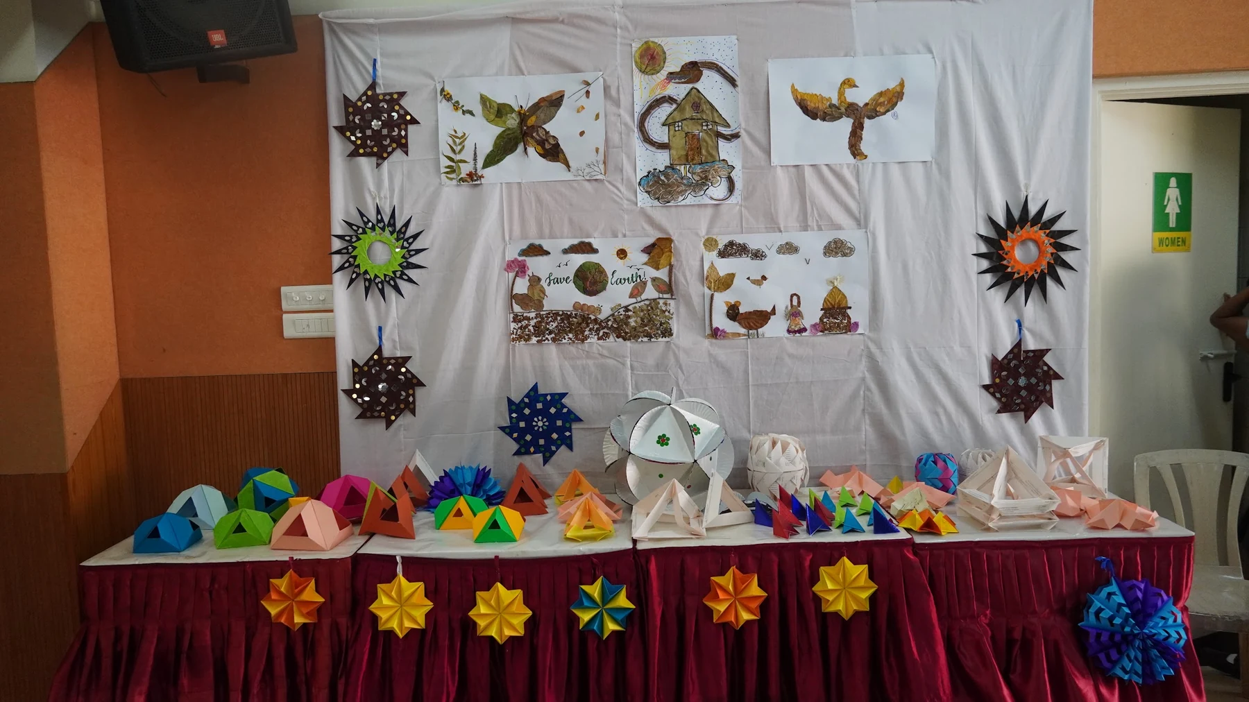 Folded paper stars, birds and boxes pinned on a white cloth above a table of paper forms