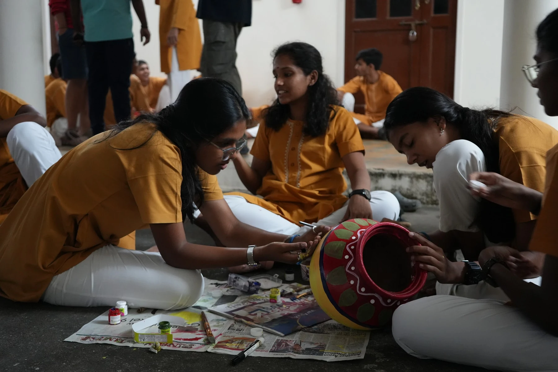 The same red pot a moment later, a student leaning in to paint along its rim