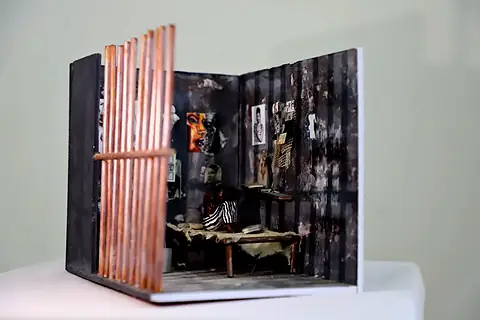 A model room seen through wooden bars, its walls covered in small pictures