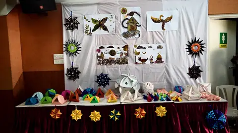 Folded paper stars, birds and boxes pinned on a white cloth above a table of paper forms