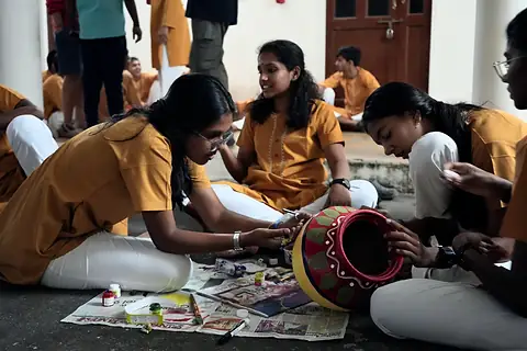 The same red pot a moment later, a student leaning in to paint along its rim