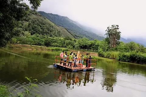 A raft carrying the Ganesh murti crossing a lake below cloud-covered hills