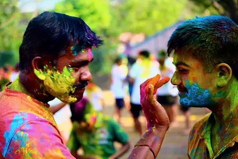 A hand pressing colour onto a student's cheek, both faces already bright with it