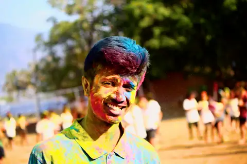 A student's face covered in blue, pink and yellow colour, smiling in low sunlight