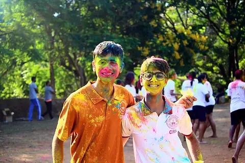 Two students standing together, faces streaked with pink and yellow colour