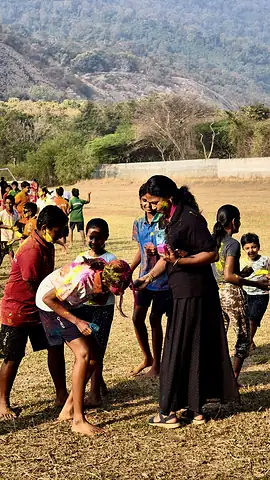 Students playing with colour on a dry field, rocky hills behind them