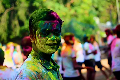 A student looking into the camera, face coated in green and pink colour