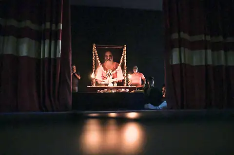 A dark hall with a portrait on stage lit only by lamps before it