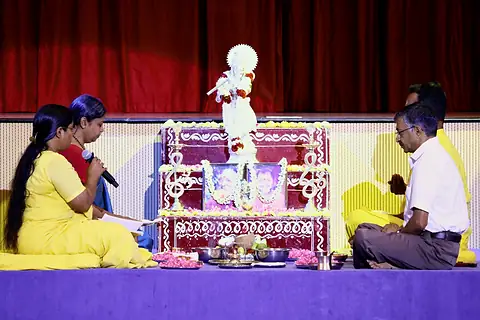 Teachers seated on either side of a flower-decked altar with a white Krishna murti