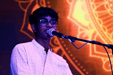 A student singing at a microphone before a red and gold projected mandala