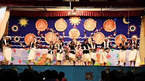 Students in white mundu and dark tops dancing on a stage hung with painted suns