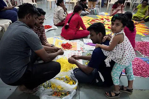 Hands sorting marigold and rose petals on the floor beside a half-laid pookalam