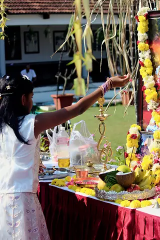 A girl placing an offering on an altar hung with sugarcane, marigold garlands, fruit and a brass lamp