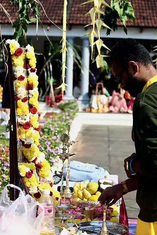 A teacher lighting lamps at an altar hung with sugarcane and marigolds in a sunlit courtyard
