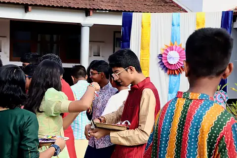 Students in festive clothes tying rakhis on one another in a courtyard