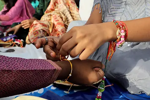 A student's hands knotting a thread rakhi on a classmate's wrist