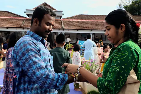 A student tying a rakhi on a teacher's wrist in the courtyard