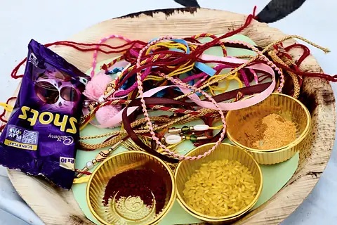 A leaf plate holding thread rakhis, red roli, yellow rice and chocolates