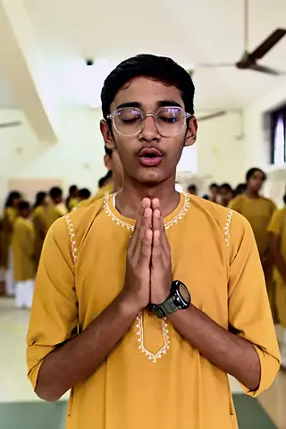 A student in a yellow kurta with palms joined