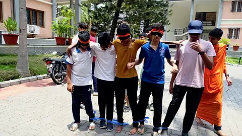 Students standing in a row in a courtyard wearing coloured bands, with a person in saffron beside them