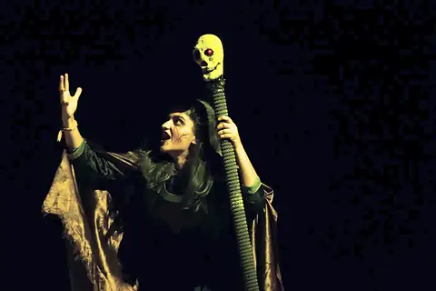 A performer with a staff under yellow stage light during Masquerade