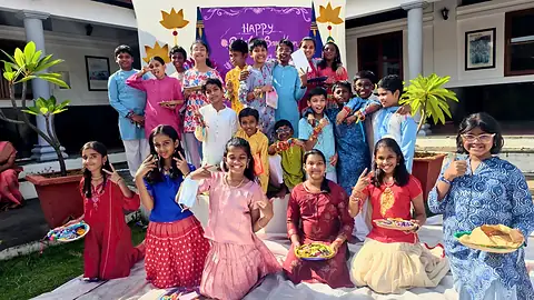 Students in festive clothes kneeling on the grass holding plates, with a group standing behind them