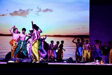 An ensemble in bright dhotis dancing before a sunset backdrop
