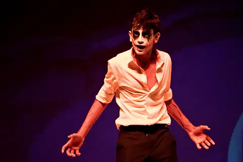 An actor in white skull face paint under orange light, hands open