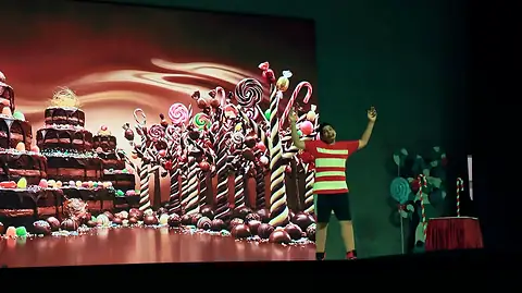 A lone actor in a striped shirt beside a projected landscape of chocolate and candy canes