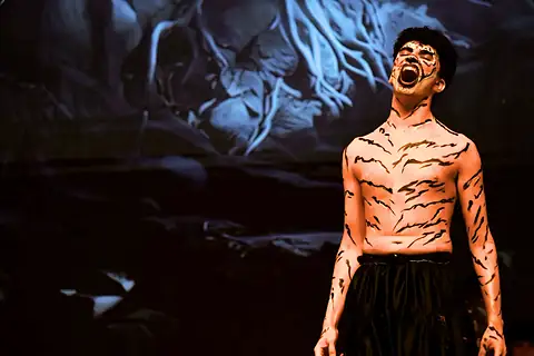 An actor in tiger body paint roaring, head thrown back