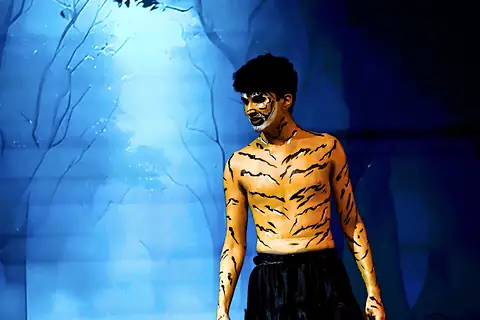 An actor in tiger body paint under blue light