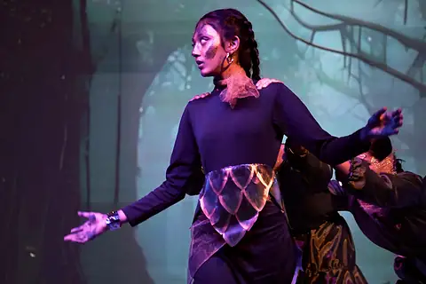 A performer in purple with glowing patterns, arms held out under violet light