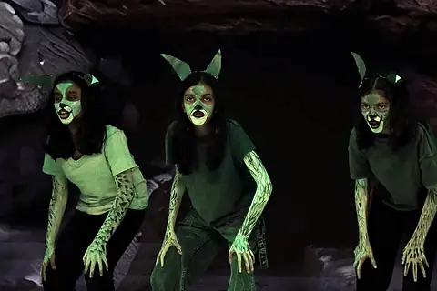 Three actors made up as wolves, crouching in green light