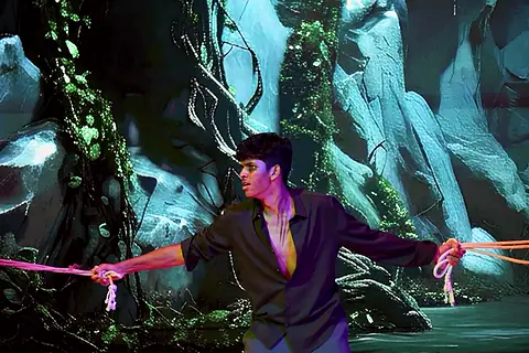 An actor tied with pink rope before a blue cavern backdrop