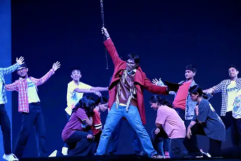 The ensemble dancing under blue light around an actor raising a staff