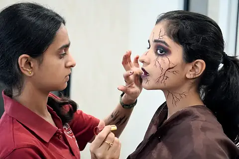 Backstage: a student painting cracks onto a cast member's face