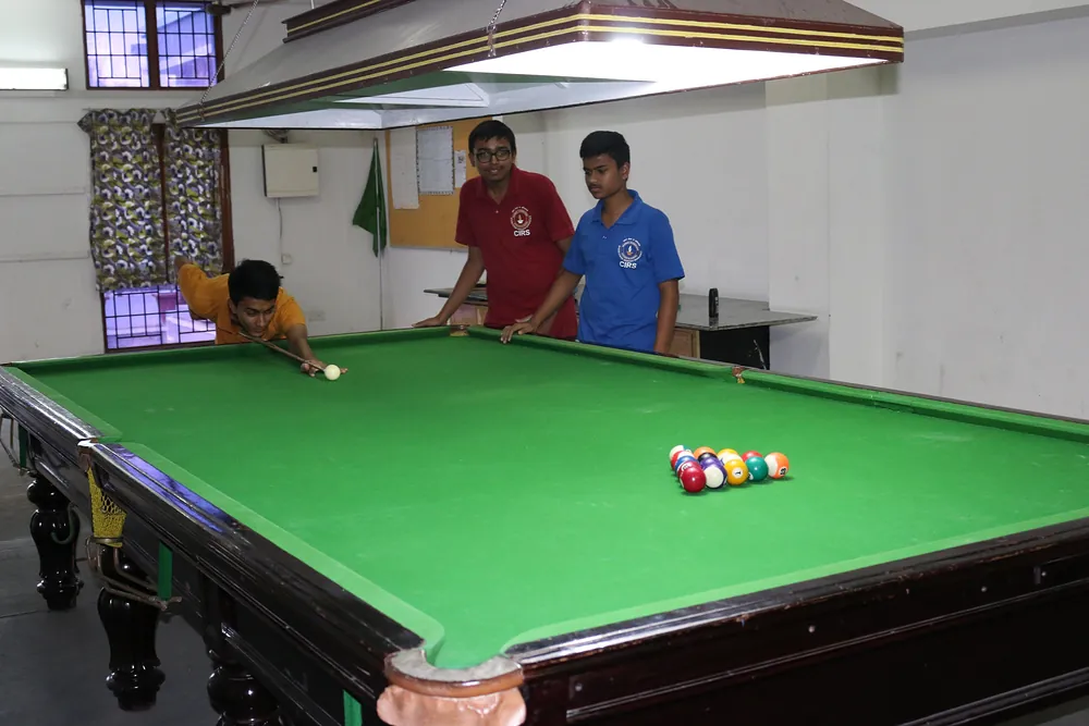 A student lining up a shot at a billiards table while two friends watch