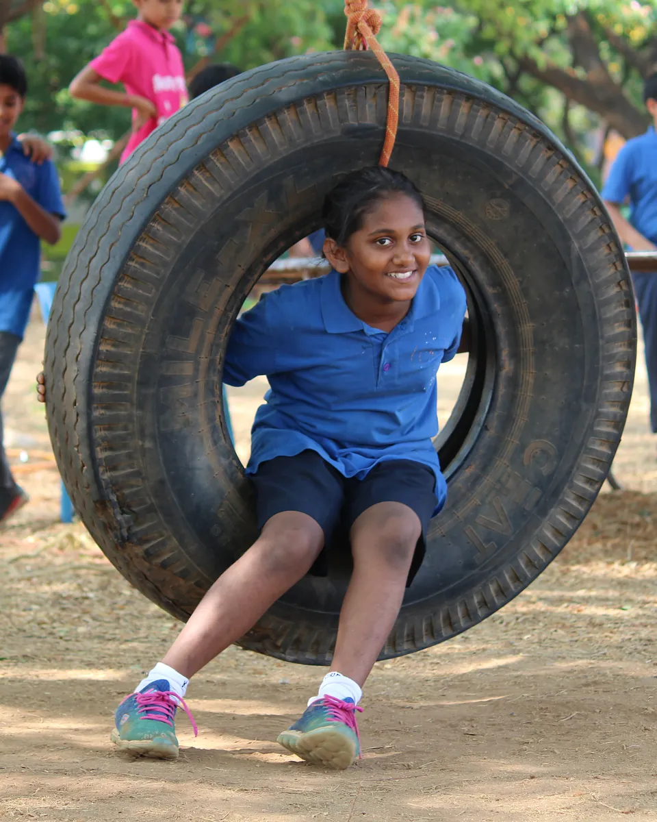 A junior student laughing as she swings through a hanging tyre, friends walking behind