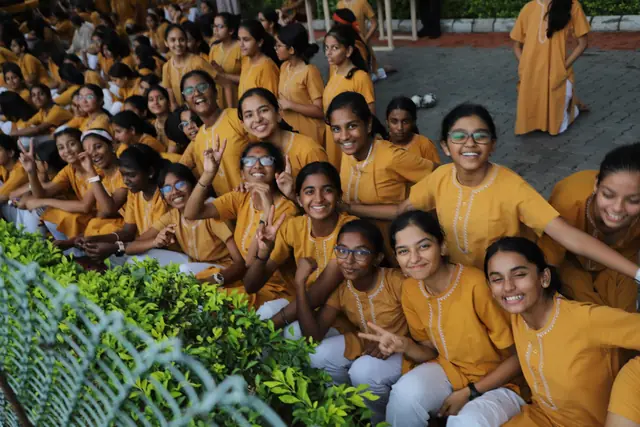 Girls in saffron kurtas seated close together on the bank, cheering