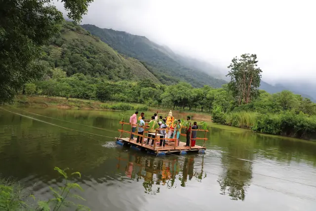 A raft carrying the Ganesh murti crossing a lake below cloud-covered hills