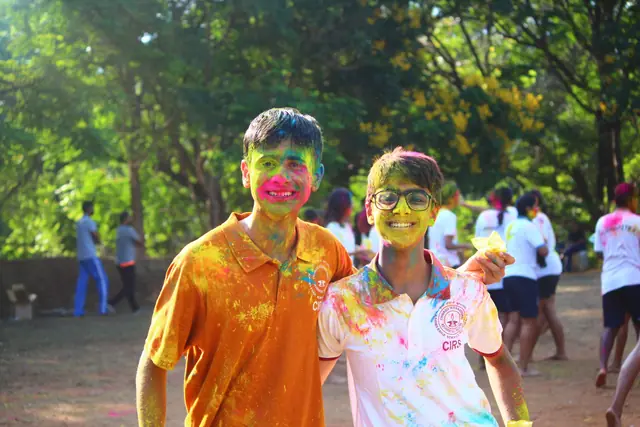 Two students standing together, faces streaked with pink and yellow colour