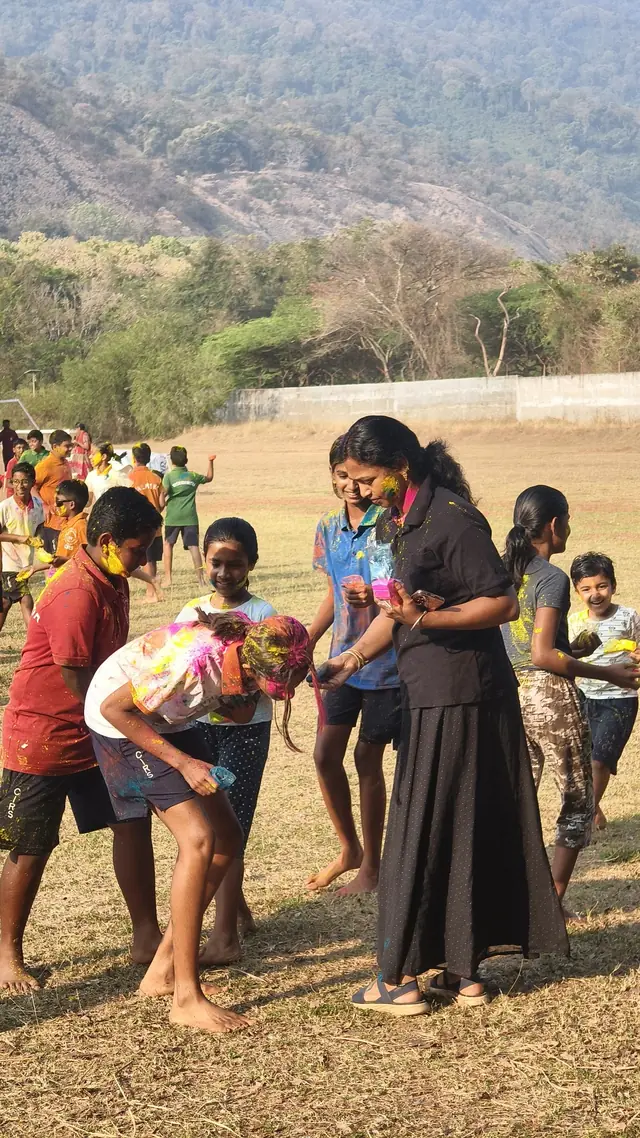 Students playing with colour on a dry field, rocky hills behind them