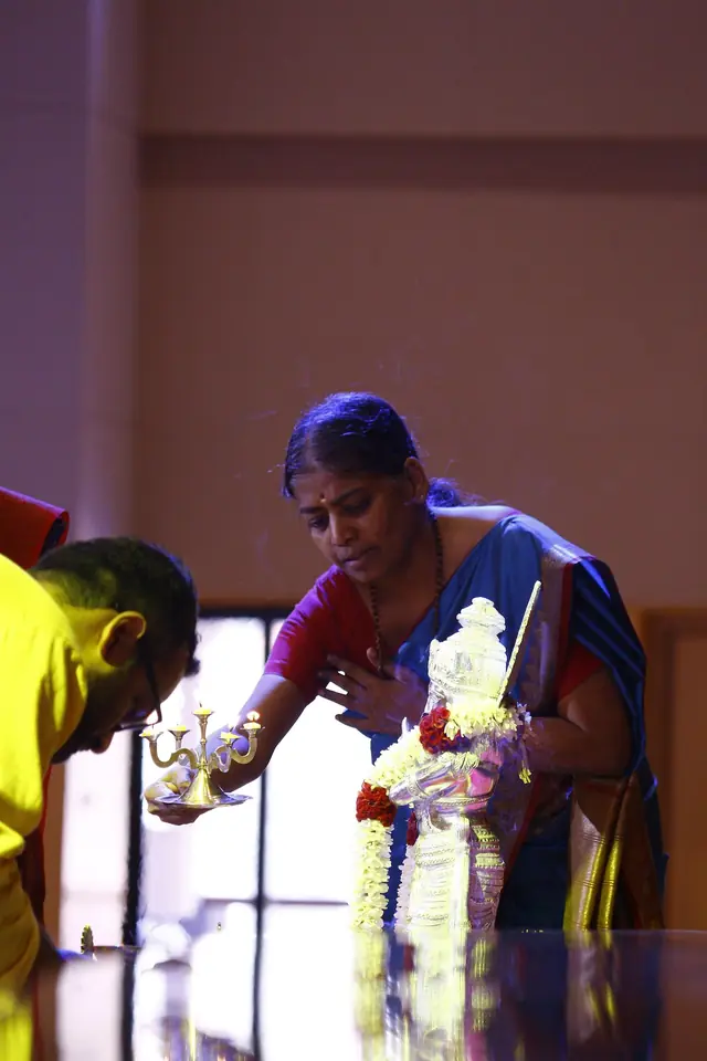 A teacher waving an aarti lamp before a garlanded murti
