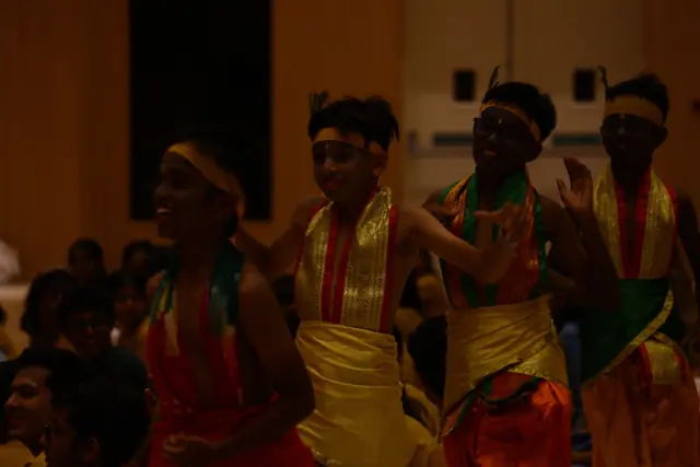 Students in red and gold costume and headbands dancing close to the audience