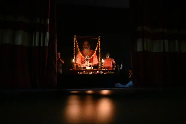 A dark hall with a portrait on stage lit only by lamps before it