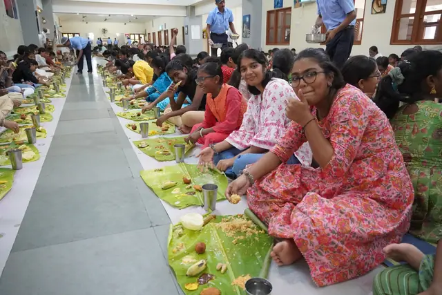Girls seated in a row on the floor with banana leaves before them, the row running into the distance