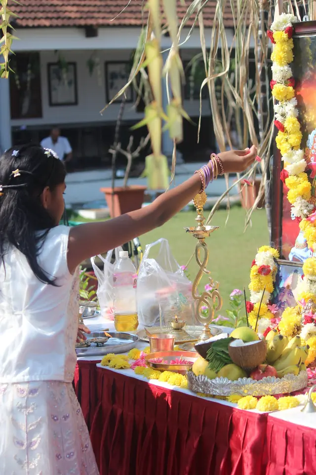 A girl placing an offering on an altar hung with sugarcane, marigold garlands, fruit and a brass lamp