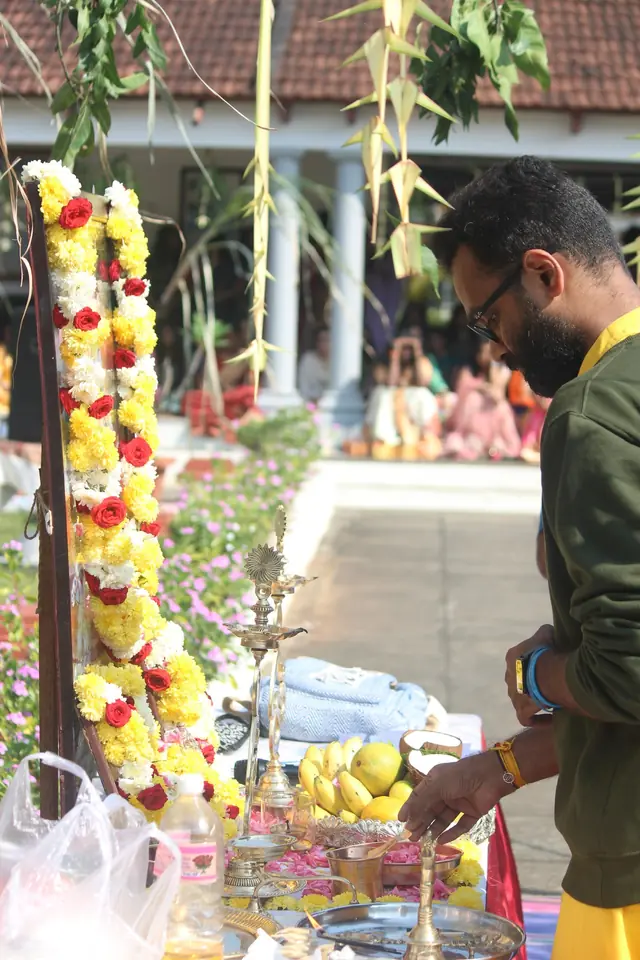A teacher lighting lamps at an altar hung with sugarcane and marigolds in a sunlit courtyard