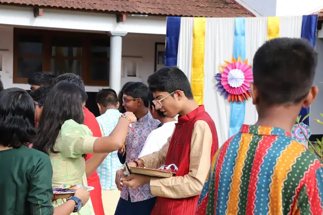 Students in festive clothes tying rakhis on one another in a courtyard