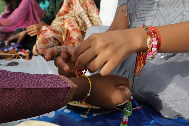 A student's hands knotting a thread rakhi on a classmate's wrist